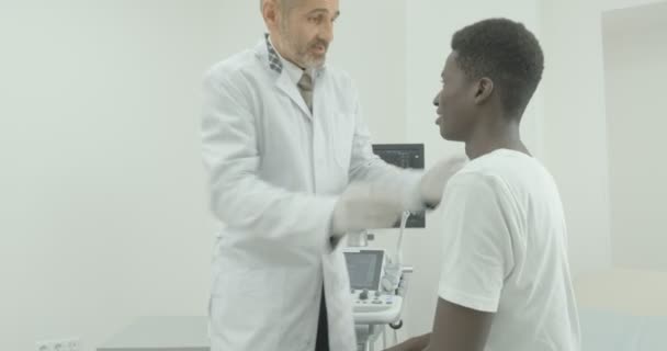 Ein Oberarzt berät einen jungen Patienten. ein Arzt begutachtet den Patienten und spricht mit ihm — Stockvideo