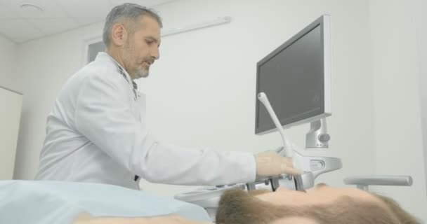 Diagnóstico ecográfico de ganglios linfáticos en el cuello. Barbudo hombre acostado en el gabinete médico . — Vídeos de Stock