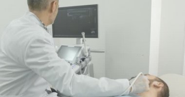 Sakallı adam yüz yan görünümü tıbbi kabine muayene yatıyor. Doktor muayene için ultrason prob kullanarak tıbbi beyaz eldiven giyiyor.