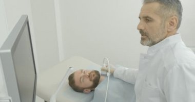 Ciddi Doktor istemci tıp kabine ile oturuyor. Sonda tutan monitör seyir terapist ultrason teşhis, yapıyor. Boyun lenf düğümlerinde inceleme uzmanı.