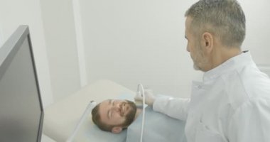 Ciddi Doktor istemci tıp kabine ile oturuyor. Sonda tutan monitör seyir terapist ultrason teşhis, yapıyor. Boyun lenf düğümlerinde inceleme uzmanı.