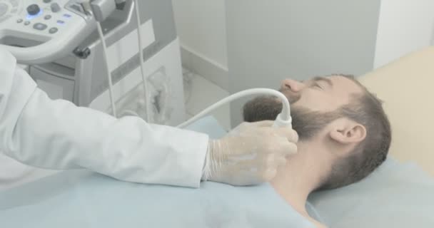 Zijaanzicht van baard man gezicht liggend op onderzoek in medische kabinet. Arts dragen in medische witte handschoen met behulp van echografie sonde voor onderzoek. — Stockvideo