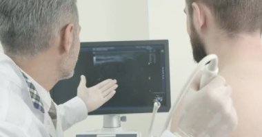 Doktor ve hasta oturan, monitör ekrana bakarak Doktor Mans omuz tarama yaparken. Özel ekipman ile tanı yaparak, ultrason prob kullanan terapist.