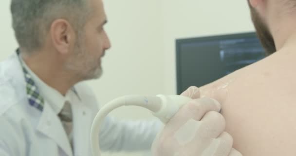 Arzt und Patient sitzen auf dem Bildschirm, während der Arzt die Schulter abtastet. Therapeut mit Ultraschallsonde, Diagnose mit speziellen Geräten. — Stockvideo
