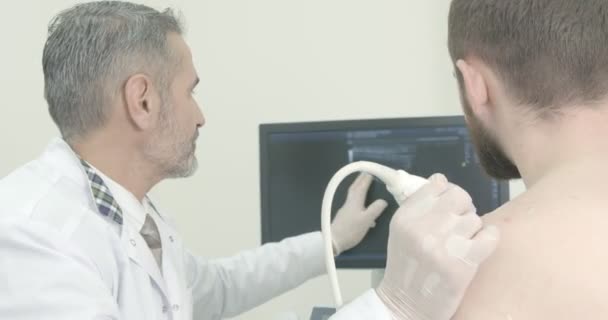 Arzt und Patient sitzen auf dem Bildschirm, während der Arzt die Schulter abtastet. Therapeut mit Ultraschallsonde, Diagnose mit speziellen Geräten. — Stockvideo