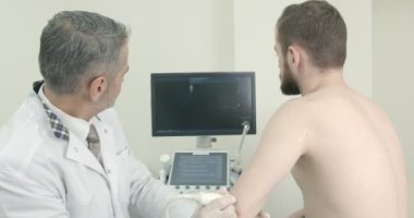 Hastaların ultrason teşhisi yapan kıdemli Doktor, eklem dirsek. Terapist tutarak cihaz ve el.