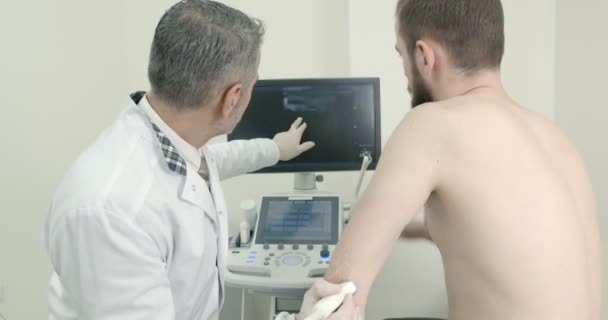 Médecin principal faisant des diagnostics échographiques de l'articulation du coude des patients. Dispositif de maintien du thérapeute et main . — Video