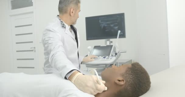Молодой африканский человек лежит в медицинском кабинете. Врач делает ультразвуковую диагностику лимфоузлов на шее . — стоковое видео