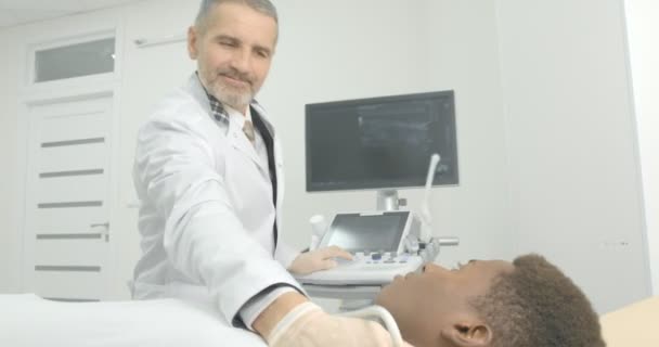 Pemuda Afrika yang terbaring di lemari medis. Dokter membuat diagnosa ultrasonik kelenjar getah bening di leher. . — Stok Video