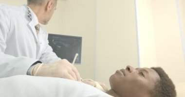 Genç Afrikalı adam sağlık kabininde yatıyor. Doktor boyun lenf nodlarının ultrason teşhis yapmak.