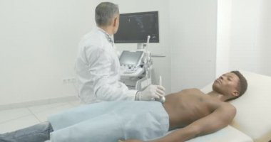 Doktor ultrasonik aparat ile genç bir Afrikalı adamın göbeğini kontrol ediyor. Çıplak gövde ile yatan Afrikalı hasta