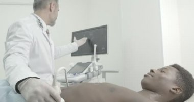 Doktor ultrasonik aparat ile genç bir Afrikalı adamın göbeğini kontrol ediyor. Çıplak gövde ile yatan Afrikalı hasta