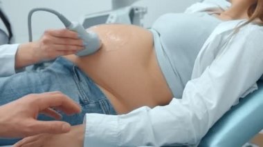 Yakın çekim, doktorun hastanede hamile bir kadına ultrason taraması yapıyor. Doğum doktoru gelecek anne göbek üzerinde dönüştürücü hareket.
