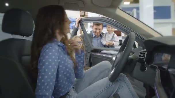 Šťastná žena sedí v křesle u řidiče v drahém autě a na zkušebním vozidle. K autu, jít za manželem s dítětem na ruce a na dívku. Usmívají se na kameru — Stock video