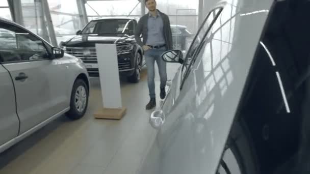 Un hombre guapo camina en una sala de exposición de coches, elige un coche modelo. El concepto de negocio de automóviles, ventas de automóviles, tecnología y personas — Vídeo de stock