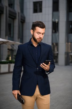 Kendine güvenen genç işadamı cep telefonu kullanarak şehirde mavi elbiseli. Adam manifatura bir mesaj outddor ofis.