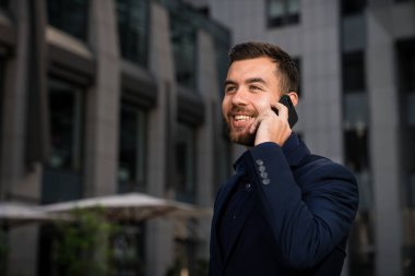 Mutlu genç işadamı bir mavi uygun fiyat şehir tarafından arama kullanarak. Outddor ofis arama ve gülümseyen bir adam.