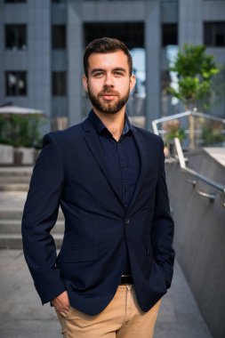 Kendine güvenen genç businessmanin mavi bir takım elbise ayakta şehirde kullanarak. İş adamı olan bir fren ve ofis dışında kamera bakıyor.