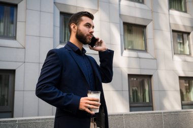 Kendine güvenen genç businessmanin bir mavi elbise arama cep telefonu şehir. işadamı içecekler kahve ve açık duvar ofisinde bir smartphone outddor konuşma.
