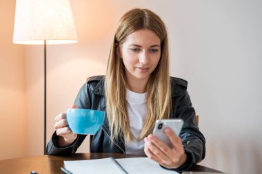 Genç kadın öğrenci masada Smartphone kullanarak ödev.