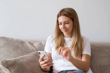 Rahat kıyafetler smartphone kullanarak ve evde kanepede otururken gülümseyen kadın portresi.