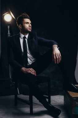 Siyah malzeme arka plan ve sinema ışığı ile bir stüdyoda oturan yakışıklı adam Portresi.