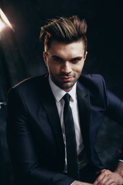 Siyah malzeme arka plan ve sinema ışığı ile bir stüdyoda oturan yakışıklı adam Portresi.