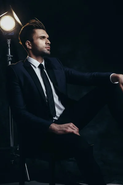 Portrait d'un bel homme assis dans un studio avec fond matériel noir et lumière du cinéma . — Photo