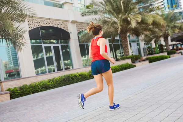 Beautiful young european woman running in marina in red top. Skyscrapers skyline in the background