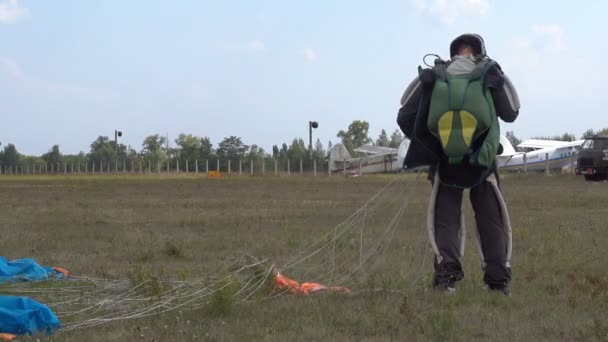 Ο αλεξιπτωτιστής στέκεται μετά την προσγείωση στο πεδίο στο γρανάζι και παίρνει μακριά το αλεξίπτωτο — Αρχείο Βίντεο