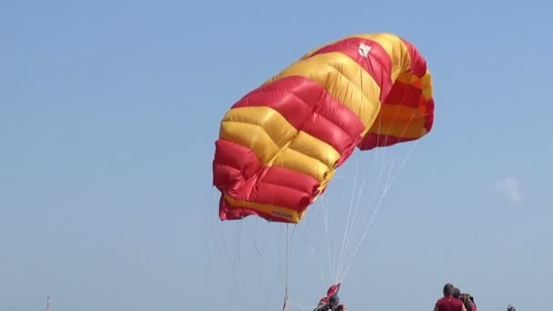 De rood-gele parachute vormen tegen de achtergrond van de blauwe hemel na de landing van de sportman-paratrooper — Stockvideo