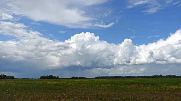 Una gran nube flotando en el cielo sobre el campo . — Foto de Stock