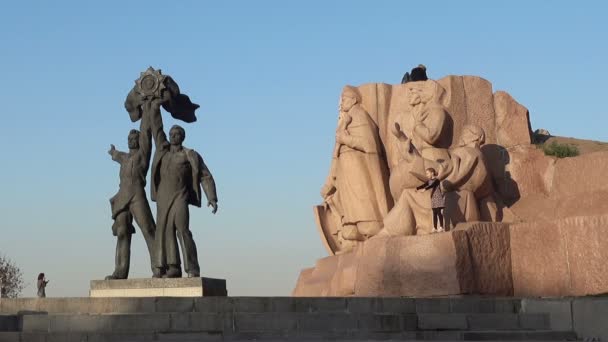 Una escultura de bronce de dos trabajadores y una escultura de granito con una escena de Pereyaslavskaya Rada cerca del arco de la amistad de los pueblos . — Vídeos de Stock