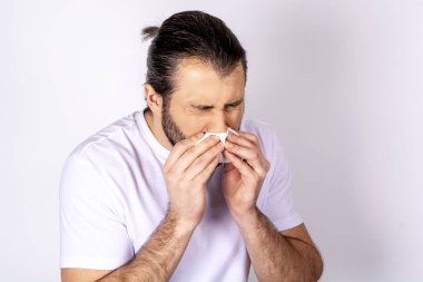 Beyaz bir arka plan üzerinde beyaz bir T-shirt yakışıklı adam hapşırma, üşütmüş