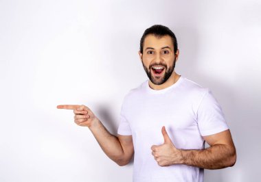 Beyaz bir arka plan üzerinde beyaz bir T-shirt yakışıklı bir adam yanına bir parmak gösterir