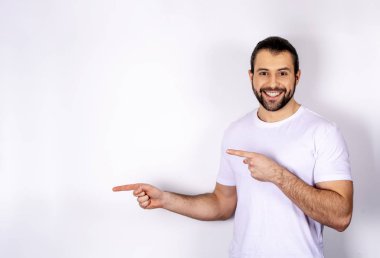 Beyaz bir arka plan üzerinde beyaz bir T-shirt yakışıklı bir adam yanına bir parmak gösterir