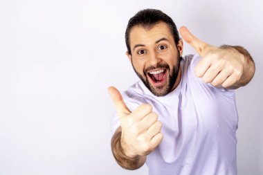 Kameraya bakarak ve seviyor gösterilen beyaz arka plan üzerinde beyaz t-shirt yakışıklı adam