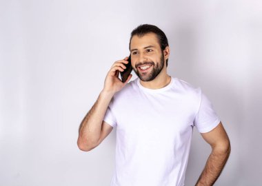 Yakışıklı adam telefonda konuşurken gülümseyen beyaz arka plan üzerinde beyaz t-shirt