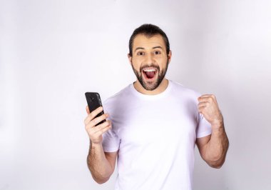 Beyaz bir arka plan üzerinde beyaz tişört gülümseyen, yakışıklı adam için bayram yapıyor, bir smartphone, elinde Sms yazıyor