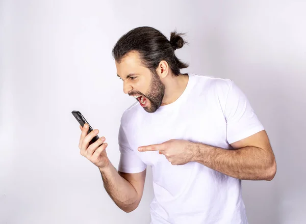 Handsome man in white T-shirt on white background screaming into the phone, angry