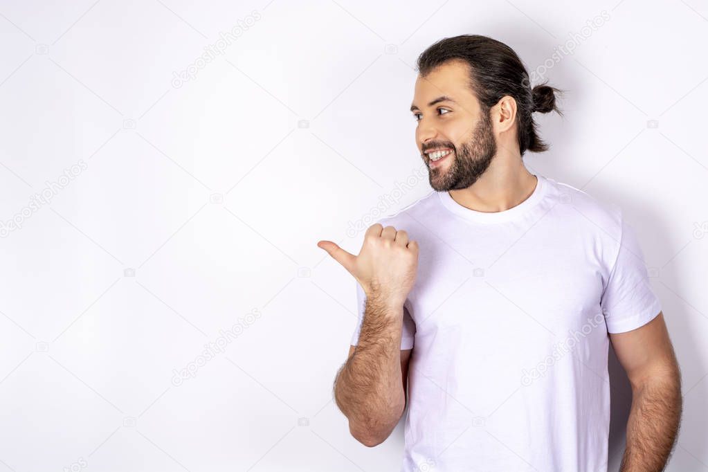 A handsome man in a white T-shirt on a white background, shows a finger to the side