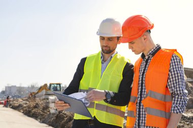 Erkekler, mühendisler, kask işçiler, birlikte bir inşaat alanında kendi yönetici ile, çizimler bakıyor, onarımlar