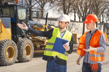 Erkekler, mühendisler, kask işçiler, birlikte bir inşaat alanında kendi yönetici ile, çizimler bakıyor, onarımlar