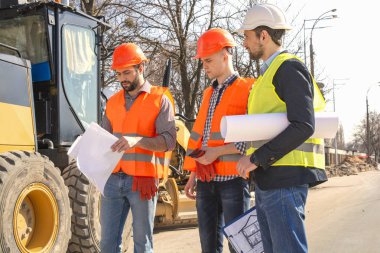 kask erkek işçiler mühendisleri buldozer ve ekskavatör yakınındaki çizimleri izliyor