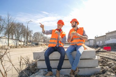 iki işçi Kasklar Öğle Yemeği, dinlenme, beton levhalar üzerinde oturmak