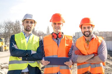 kaskları erkek işçiler mühendisleri kamera içine bakmak ve gülümseme, bir inşaat alanında