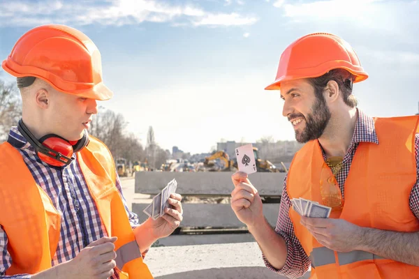 two man working engineers in helmets playing cards at a construction site