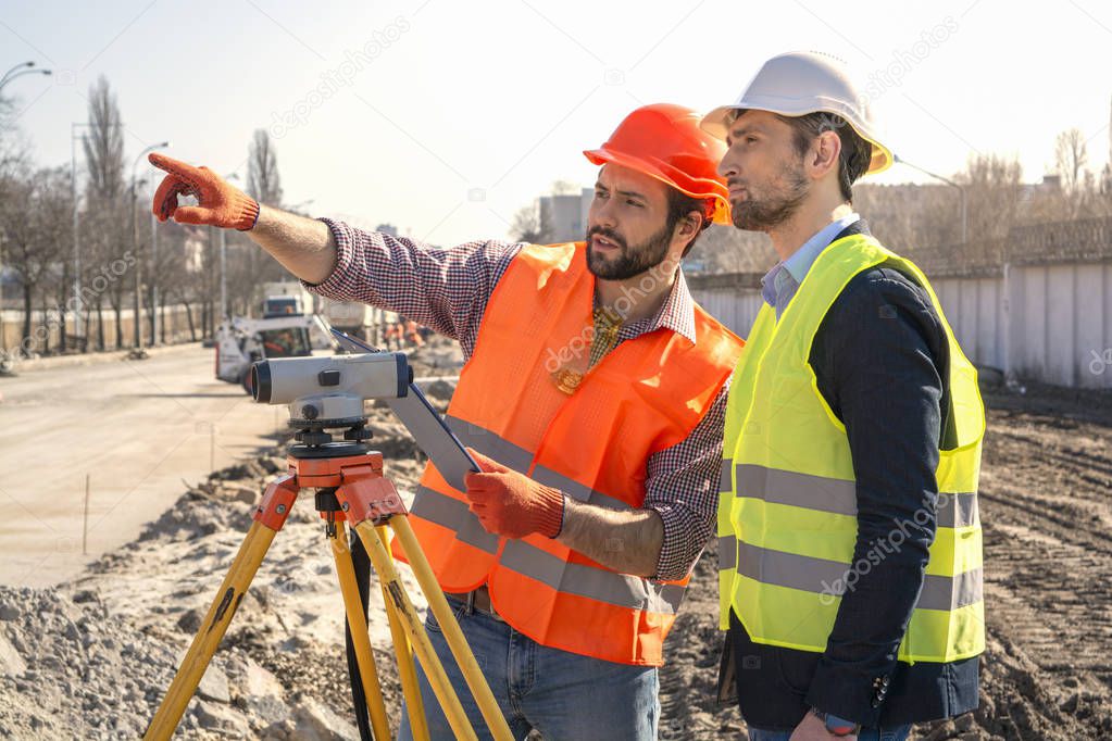 male surveyor engineer with a device working on a construction site in a helmet