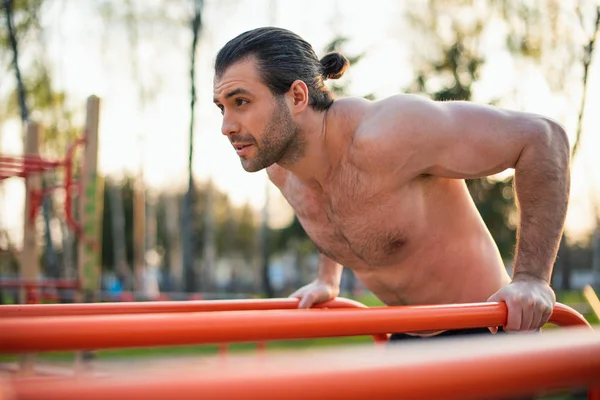 male athlete, torso with muscles, outdoors training, smiling, horizontal bar