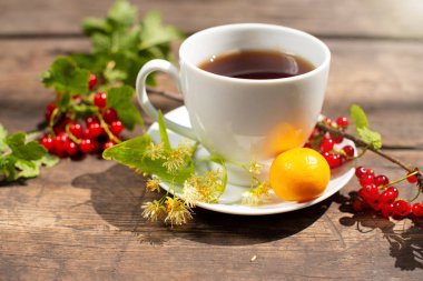 Beyaz bardakta çay, ahşap bir masada, bir çileğin etrafında, çilek, nane